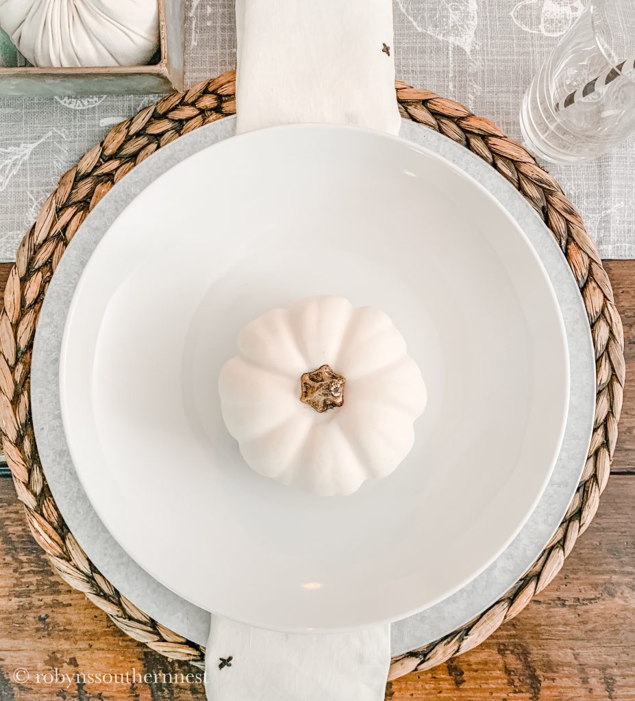 a view of place setting with woven chargers, galvanized charger and plate with white pumpkin on the center of the plate 