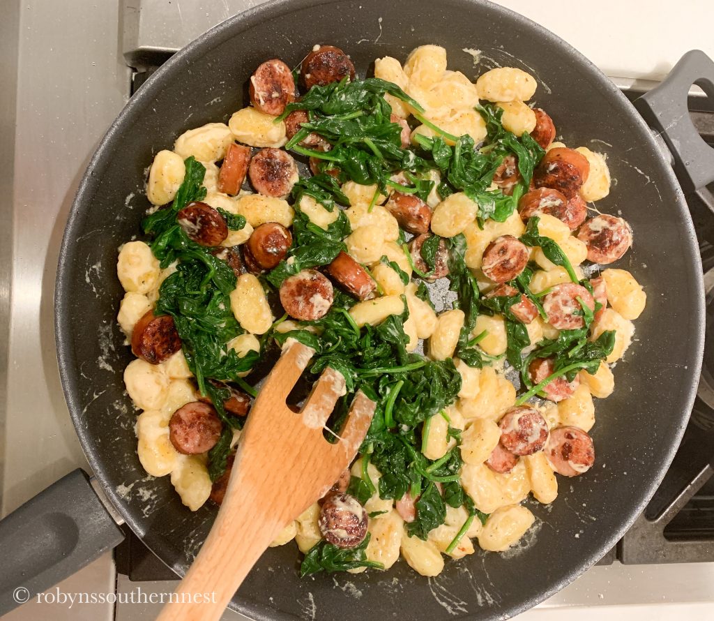 apple sausage and parmesan gnocchi with spinach stirring in a pan 